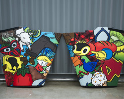 Emirates Team New Zealand's AC72, NZL5 king post fairing with Kiwiana graphics. Basket of Kina, Lamb, Fern, Gumboot, Rugby ball, Corrugated iron sheet, Tiki, Paua shell, Kiwi sign, Pineapple lumps, Frosty Boy, Jet plane lolly, Pohutukawa, Tomato sauce bottle, Kumara, Jandal, Swandry, Kiwi fruit, Buzzy Bee, Number eight fencing wire, Pukeko, Four square, Hokey Pokey Ice cream cone