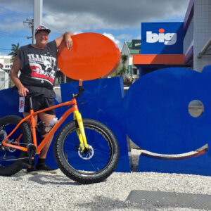 Ross Hall standing next to BIG sign outside of premises, with large orange mountain bike