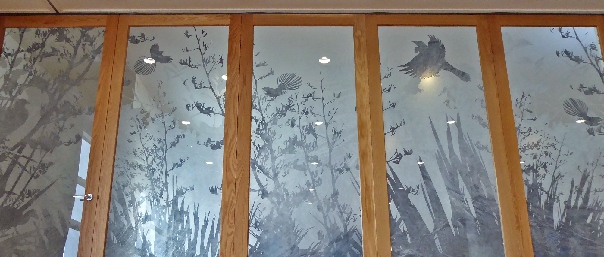 Detailed silhouette design of NZ native birds flying around a flax bush - on a window