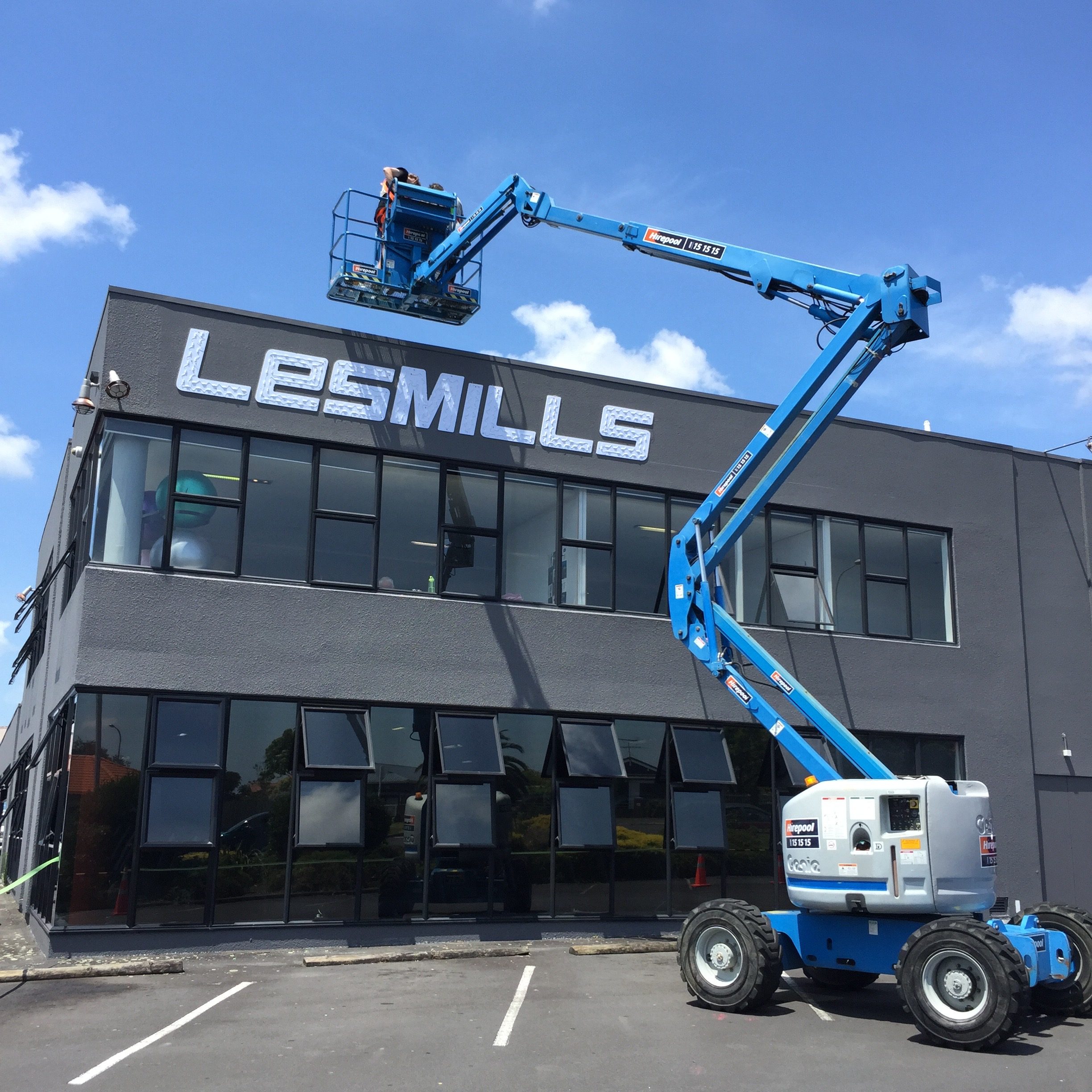Les Mils signage being attached with blue cherry picker