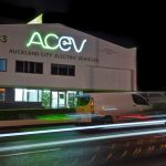 Light trail of AC EV frontage, wth green and blue building signage lit