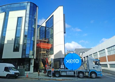 Truck carrying Xero sign parked outside of building, stabilising itself, ready for crane installation