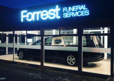 Forrest Funeral Services illuminated signage with hearse in the background